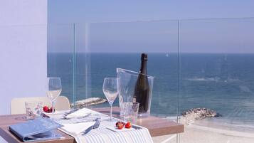 Una mesa dispuesta con una botella de champán, copas de vino y un menú en un balcón con vistas al mar.