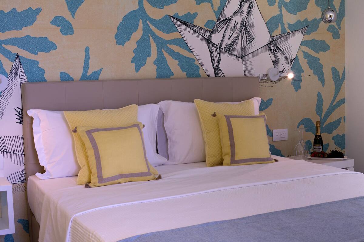 A neatly made bed with white and yellow bedding, a headboard, and a wall with a leaf pattern.