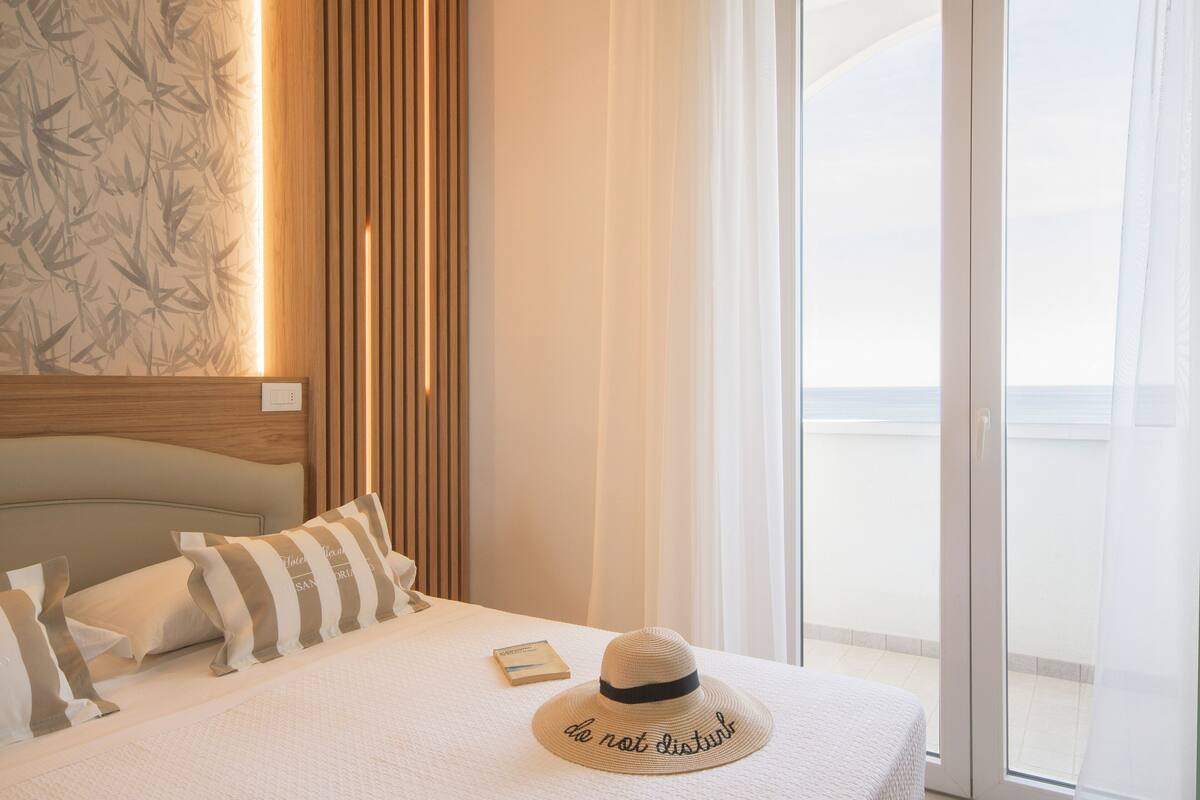 A hotel room with a bed, a hat, and a book on the bed.