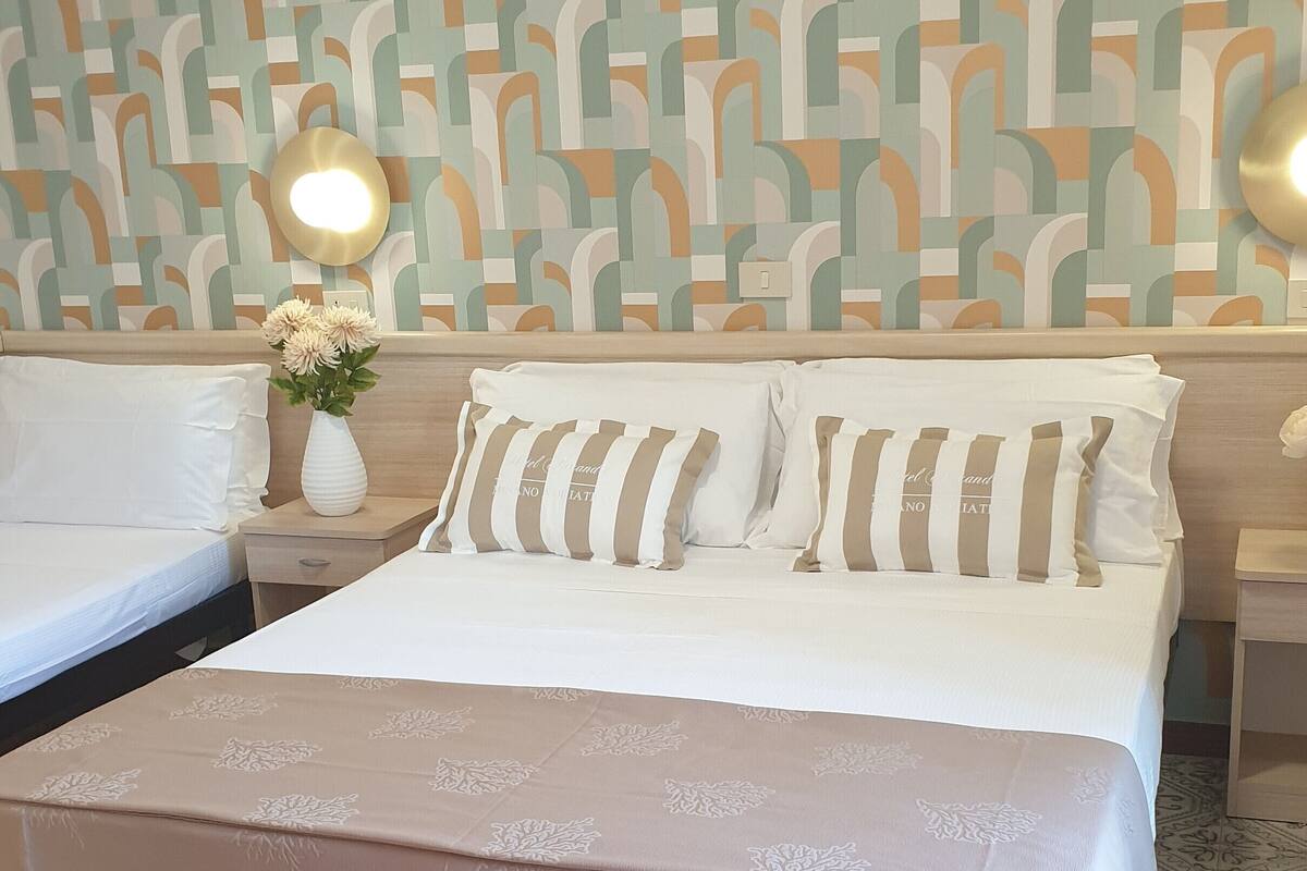 A neatly made bed with a patterned bedspread, a bedside table with a vase of flowers, and a wall with a geometric pattern.