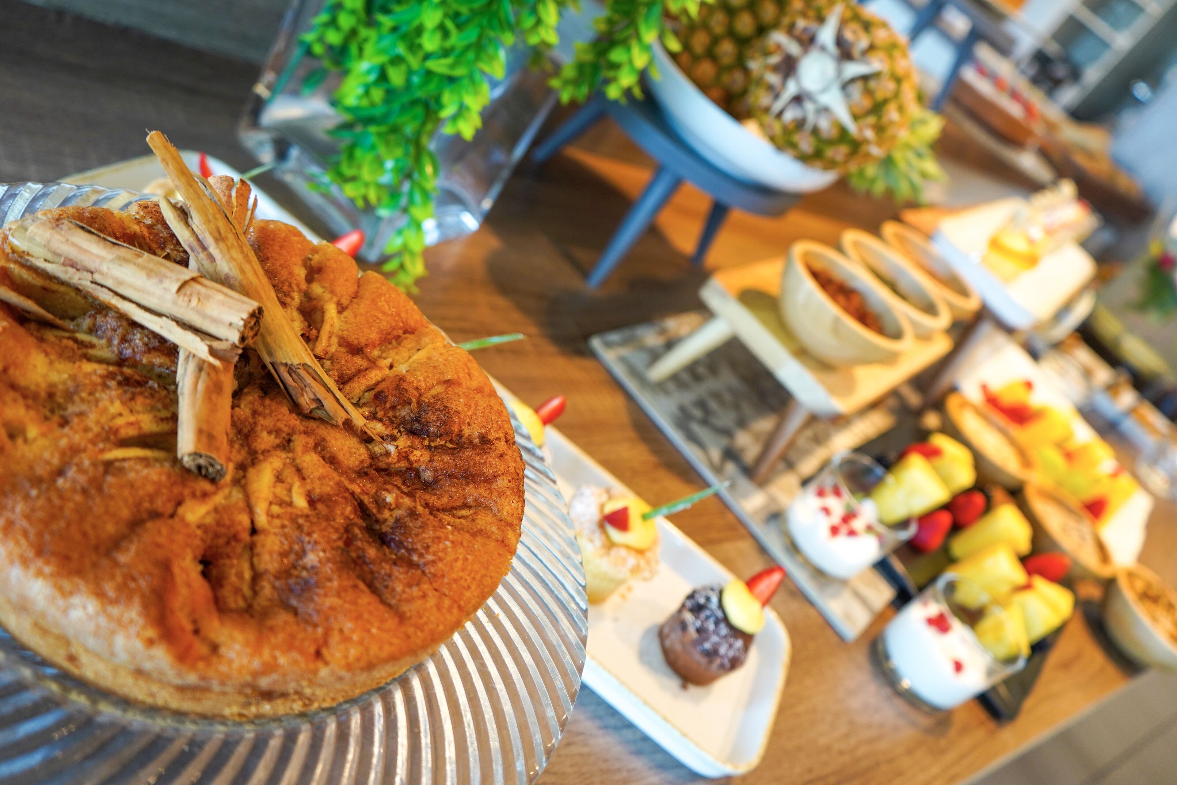 A buffet table with a variety of dishes including a large round cake, fruit skewers, and small desserts.