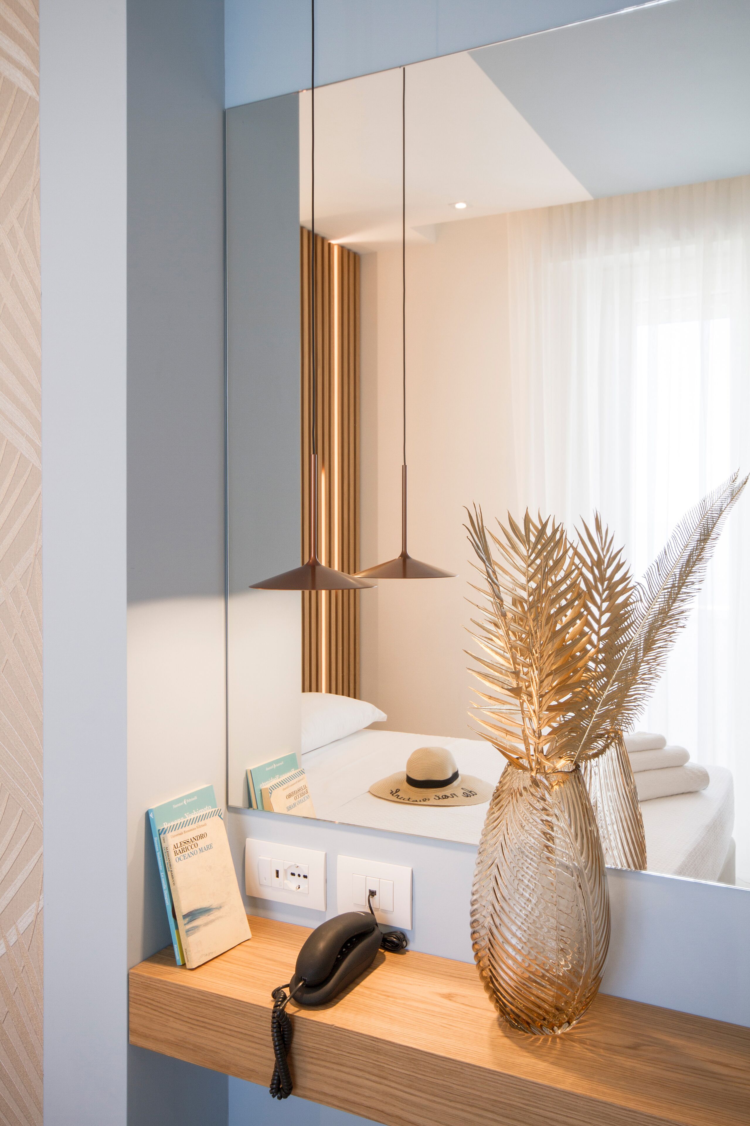 A modern bathroom with a wooden vanity, a mirror, a telephone, a decorative vase, and a towel rack.