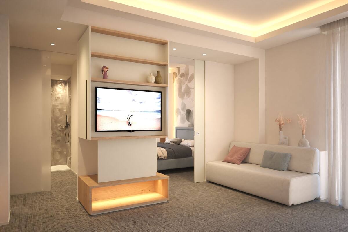 A modern living room with a flat-screen TV mounted on a wooden stand, a grey sofa with cushions, and a small table with decorative items.