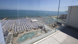 Ein Balkon mit freiem Blick auf einen Strand mit zahlreichen Sonnenschirmen und einem Schwimmbad.