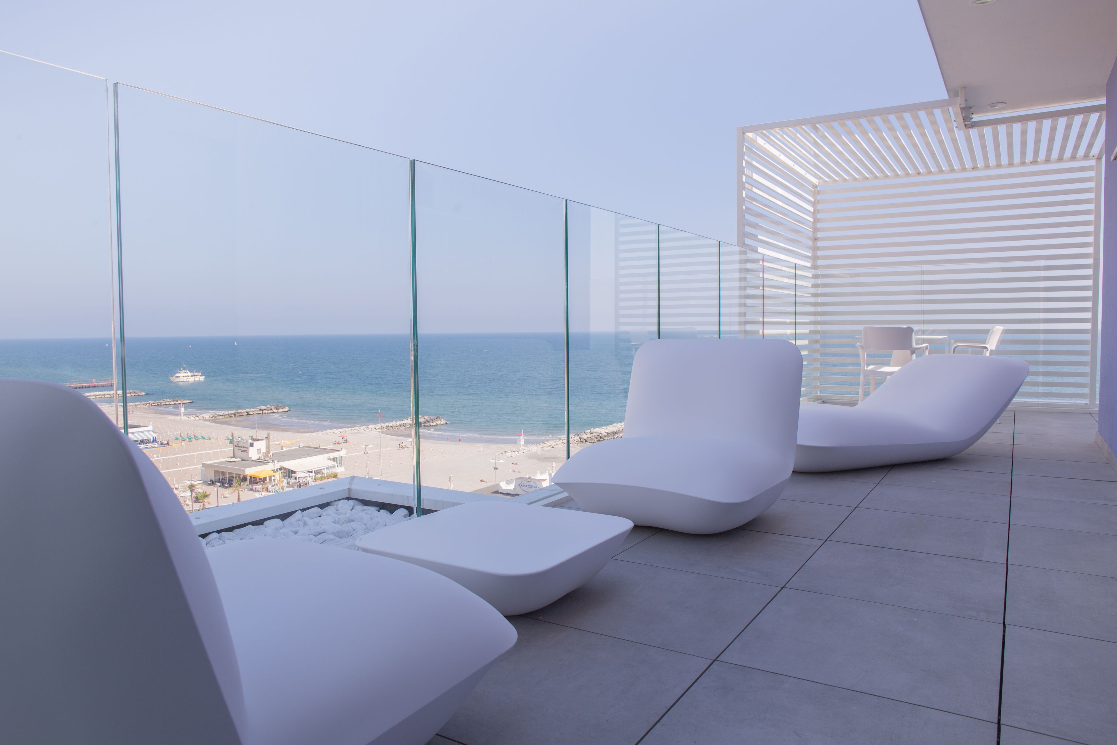 Ein moderner Balkon mit weißen Lounge-Stühlen, einer Glasreling und Blick auf Strand und Meer.