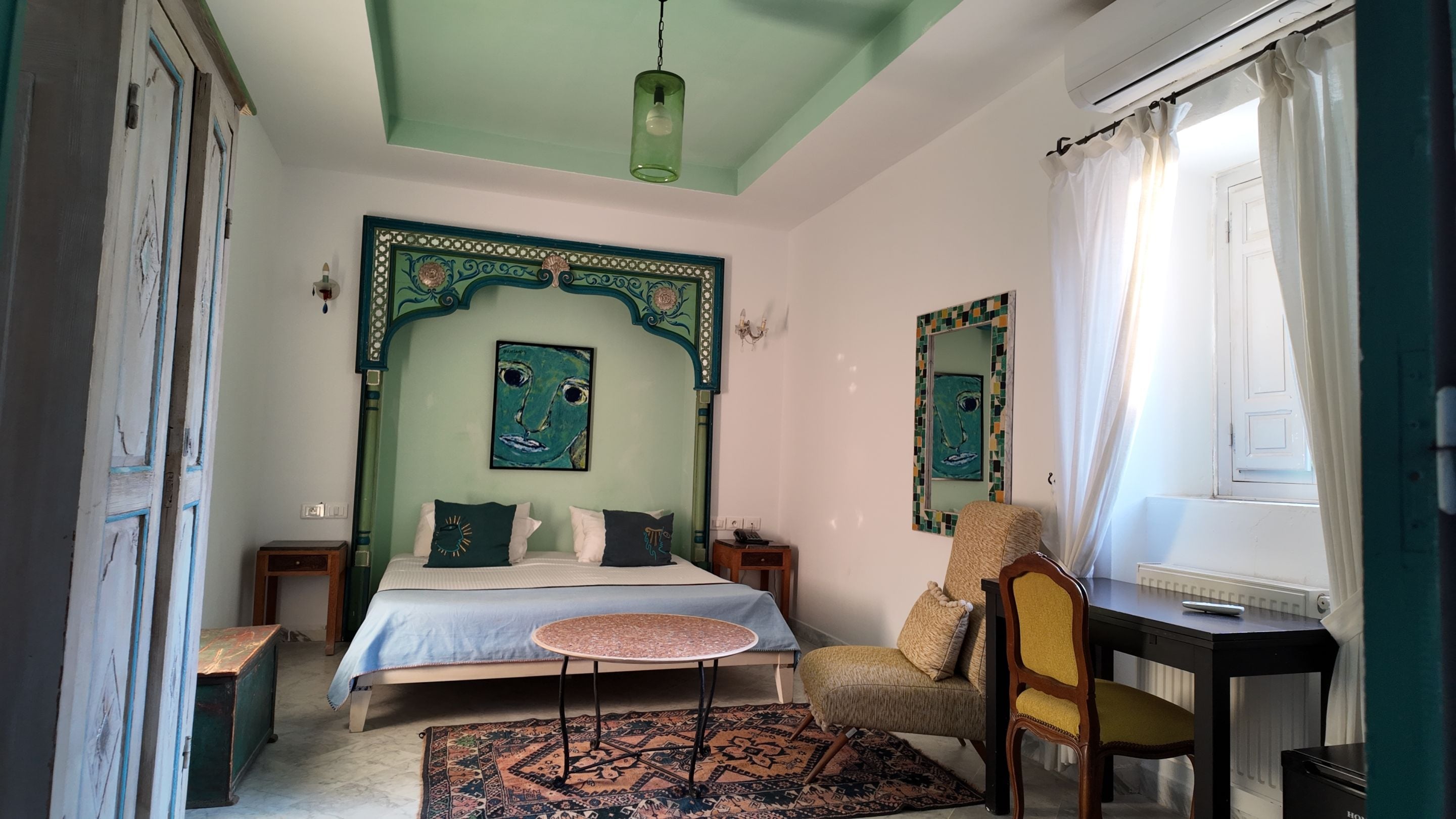 A bedroom with a bed, a chair, a table, and a window with curtains.