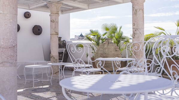 Un patio al aire libre con mesas y sillas de metal blanco, un pilar de piedra y un gran jarro decorativo.
