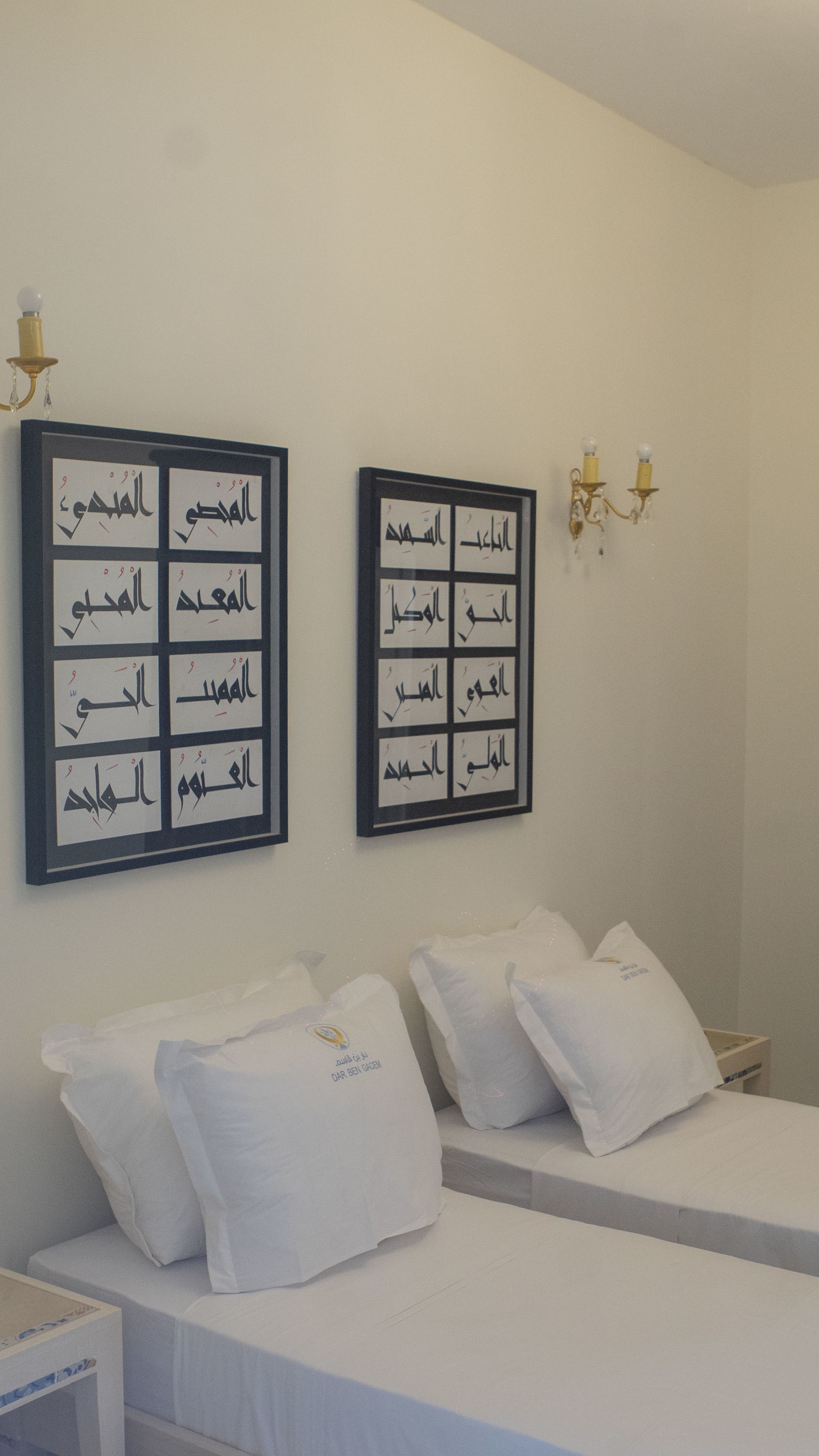 Une chambre d’hôtel avec deux lits, du linge de lit blanc et des œuvres d’art calligraphique arabe accrochées aux murs.