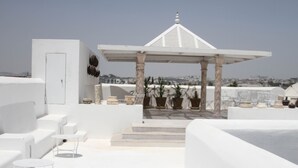 Une terrasse sur le toit, agrémentée de mobilier blanc, d’un belvédère et de plantes en pot.