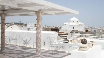 Une terrasse sur le toit, avec des chaises en métal blanc, une table blanche et un parasol blanc.