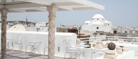 Una terraza en la azotea con sillas de metal blanco, una mesa blanca y una estructura de sombrilla blanca.
