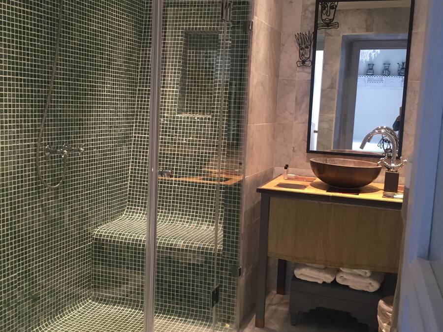 Un baño con ducha compartimentada con vidrio, tocador de madera con un lavamanos grande y un espejo sobre el lavamanos.