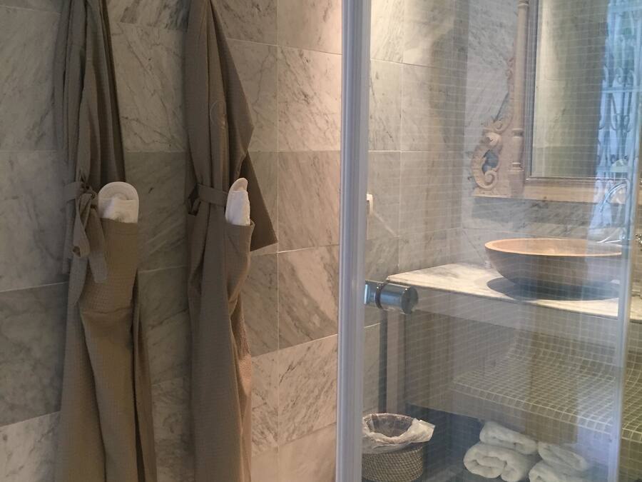 A bathroom with marble tiles, a glass shower enclosure, a sink with a bowl, and towels hanging on the wall.