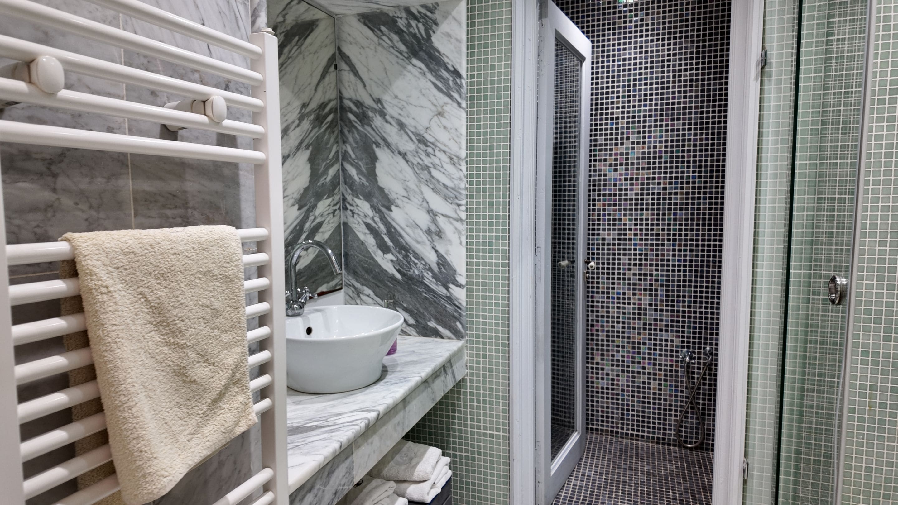 A bathroom with a white sink, a towel rack, and a shower area with a glass door.