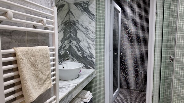 Un baño con lavamanos blanco, toallero y zona de ducha con puerta de vidrio.