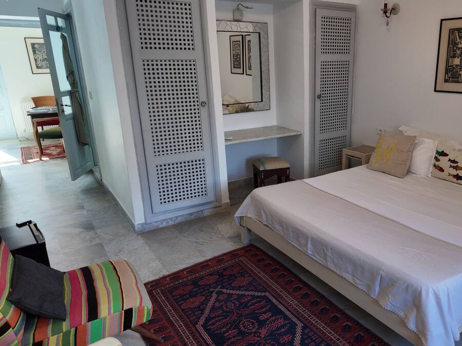 Een slaapkamer met een bed, kussens, een vloerkleed en kunst aan de muur.