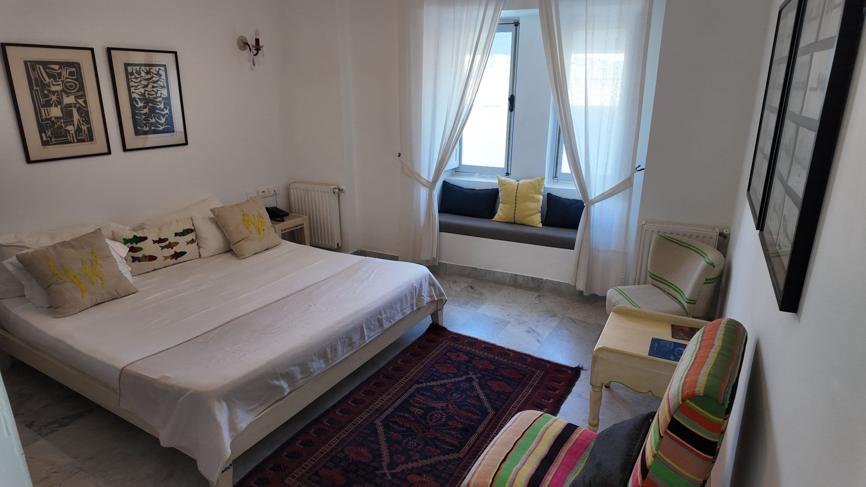 A bedroom with a bed, a window with curtains, a chair, and a small table.