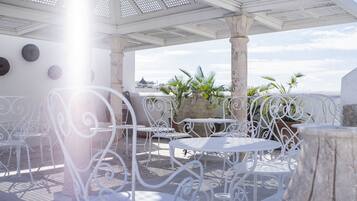 Une terrasse extérieure avec des chaises et des tables en métal blanc, des piliers en pierre et des plantes en pot.