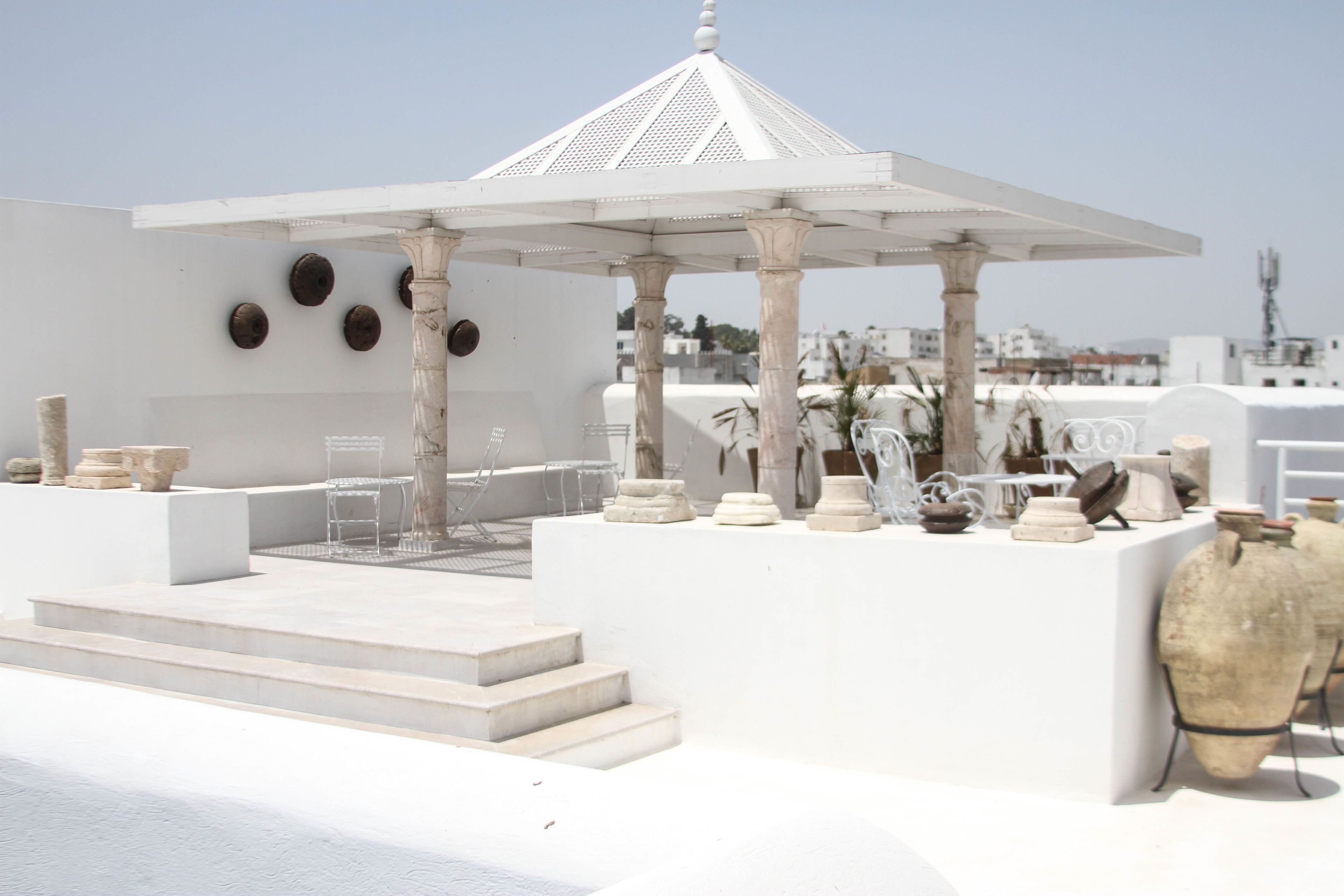 A white gazebo with columns, steps leading up to it, and various stone and ceramic objects displayed around it.
