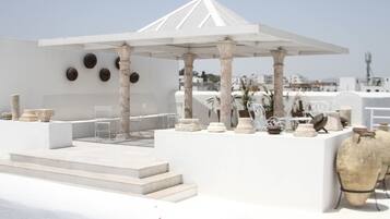 A white gazebo with columns, steps leading up to it, and various stone and ceramic objects displayed around it.