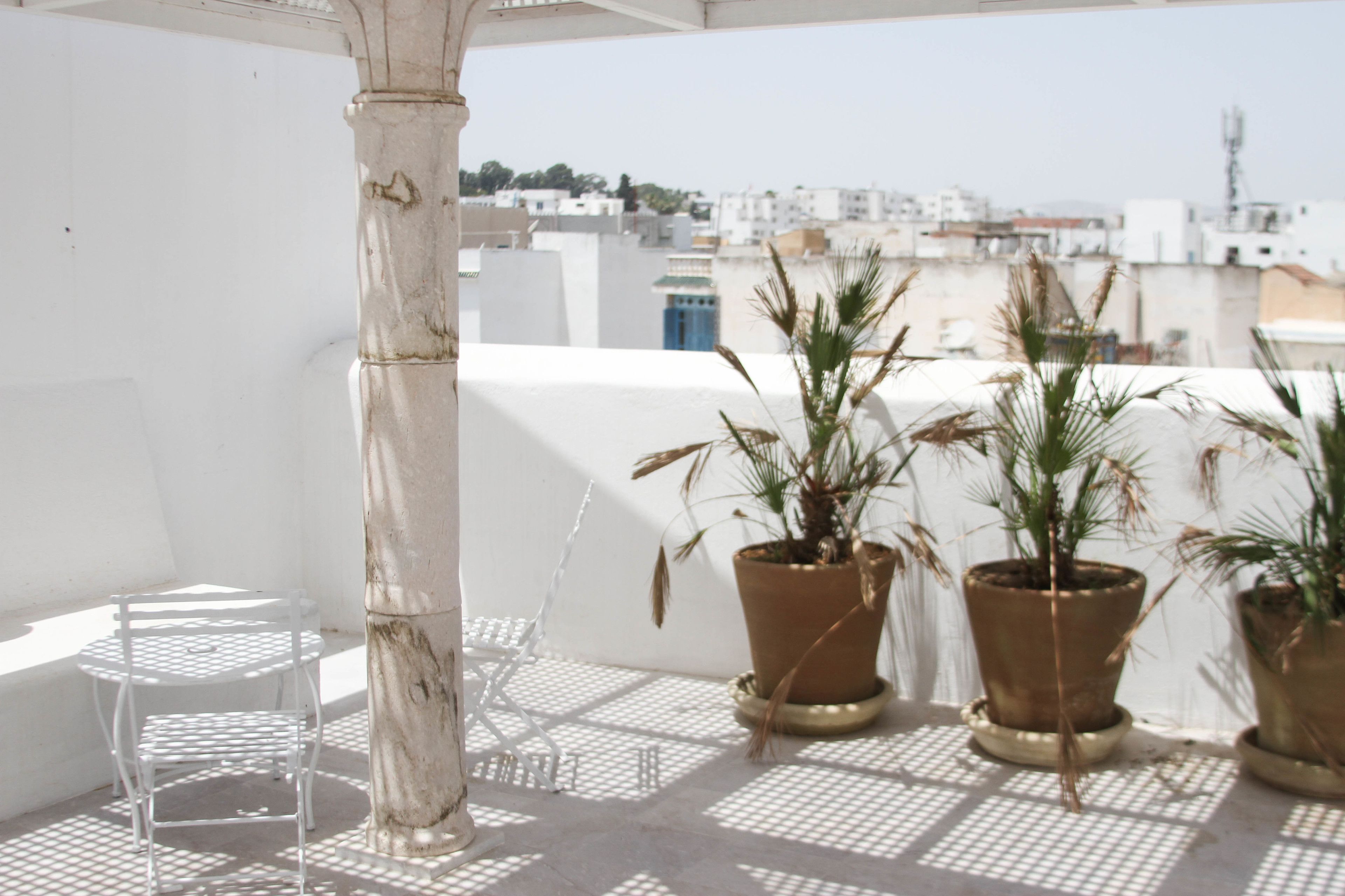A rooftop terrace with potted plants, a white chair, and a clear view of the cityscape.