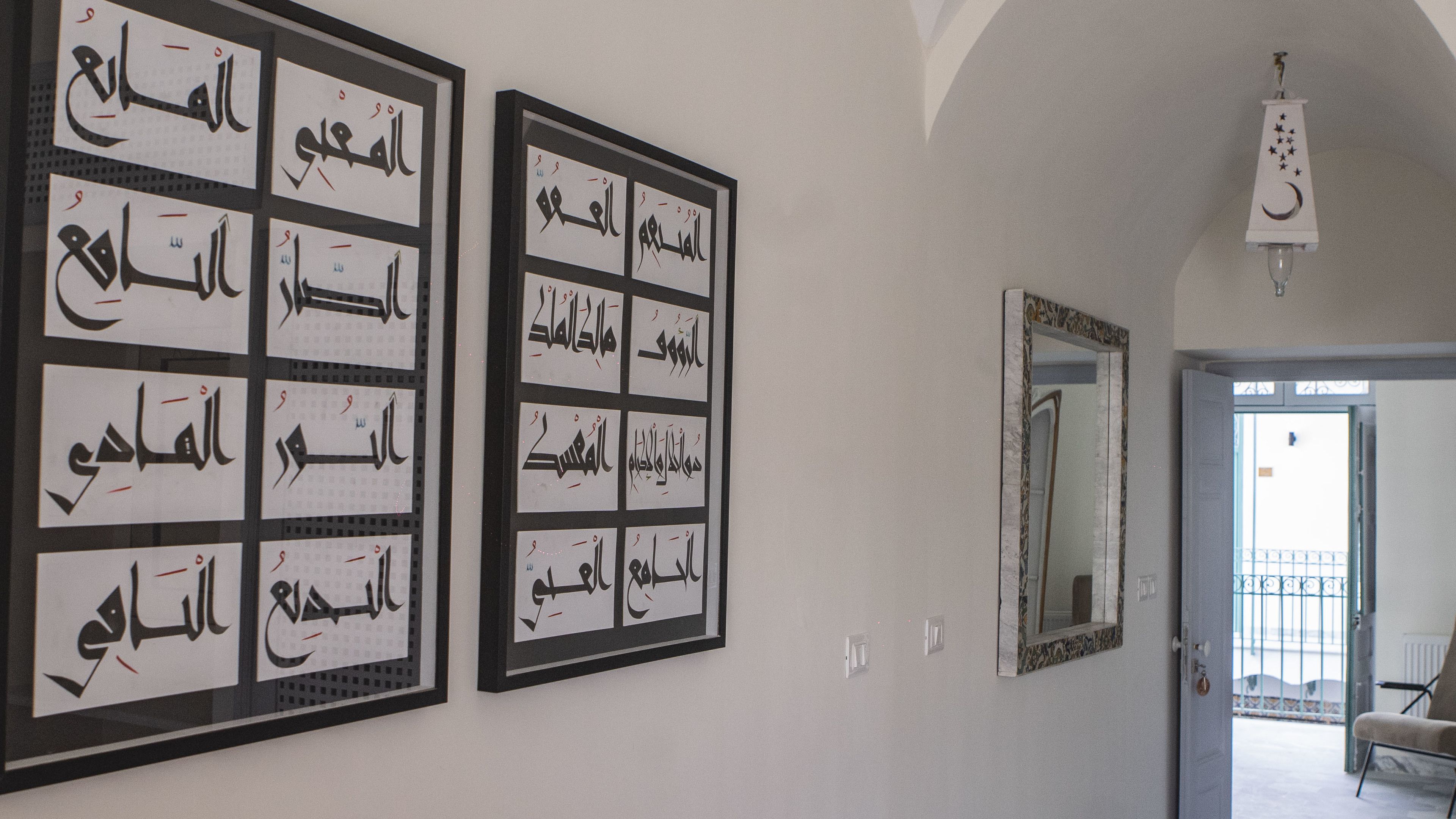 A hallway with framed Arabic calligraphy on the walls and a mirror on the right.