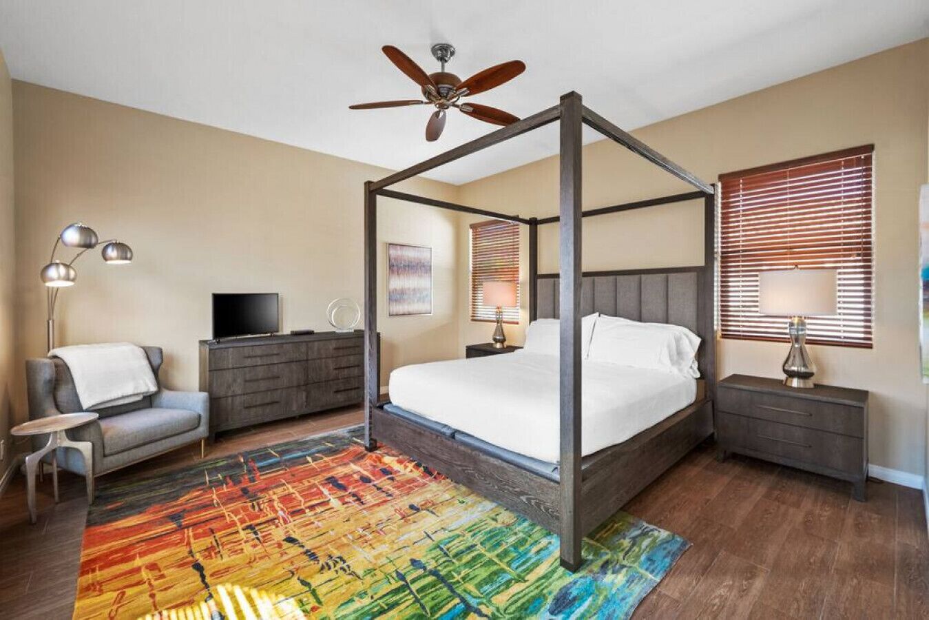 A bedroom with a four-poster bed, a television, a desk, a chair, and a colorful rug.