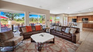 A spacious living area with a large brown leather sofa, a coffee table, and a view of a patio with outdoor furniture.