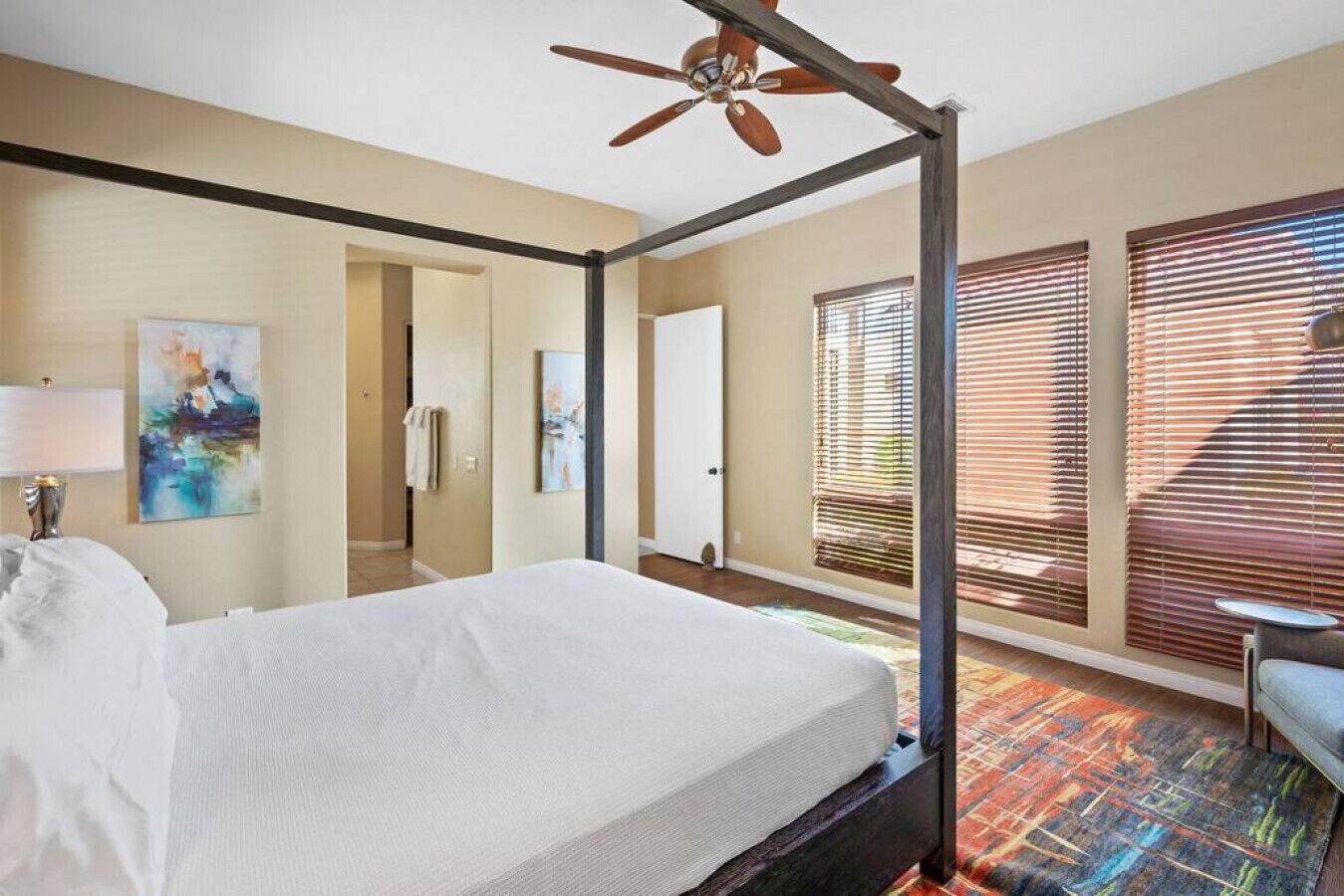 Une chambre d’hôtel avec un lit à baldaquin, un ventilateur de plafond et une grande fenêtre avec des stores.