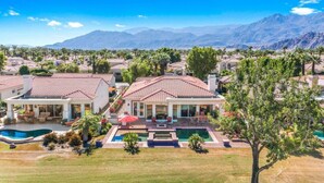 A large house with a swimming pool, surrounded by mountains.