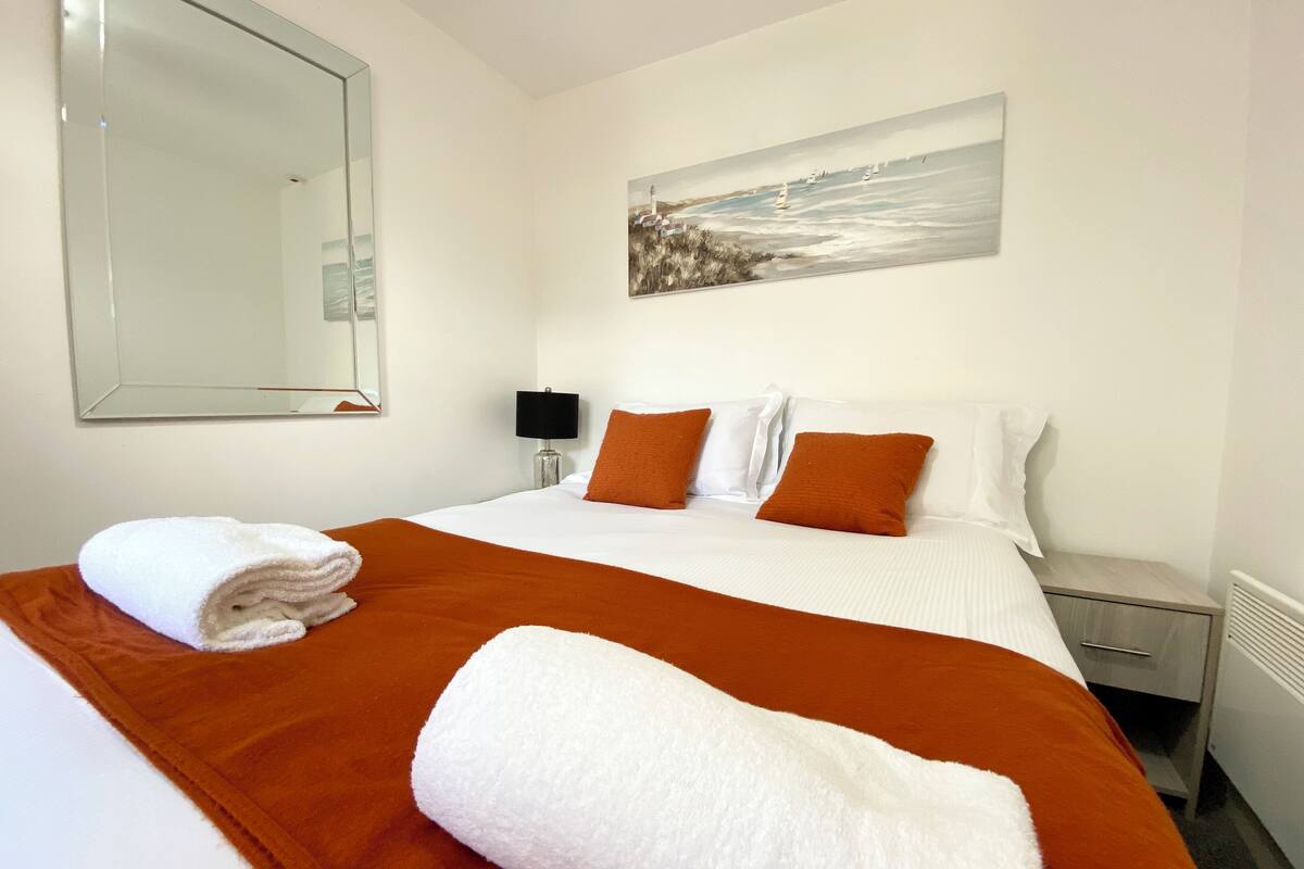 A hotel room with a bed, a painting, a nightstand, and a radiator.