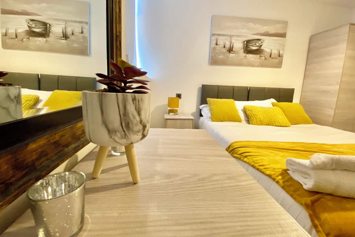 A hotel room with a bed, a nightstand, a mirror, and two paintings on the walls.