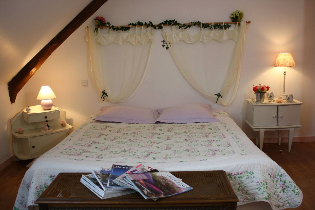 A bedroom with a bed, a nightstand, a lamp, and a small table with magazines.
