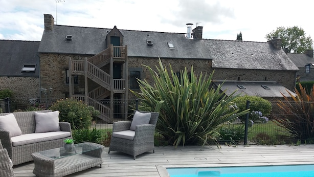 A poolside area with wicker furniture and a stone building in the background. - Les Keriaden's Maison d'hotes (Pleudihen-sur-Rance)