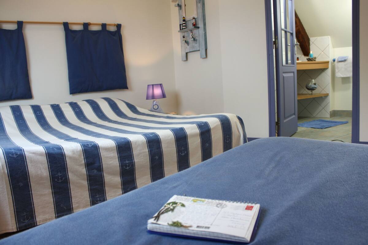 A bedroom with a bed, a nightstand with a lamp, and a door leading to a bathroom.