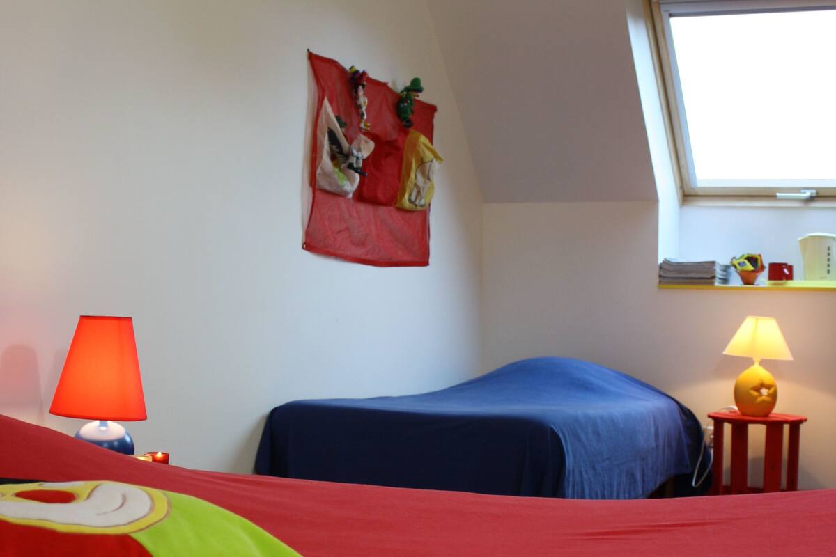 A room with two beds, a window, a lamp, and a wall decoration.