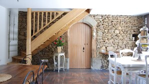 A rustic interior with a wooden staircase, stone wall, wooden door, and a dining area with white furniture. - Les Keriaden's Maison d'hotes (Pleudihen-sur-Rance)