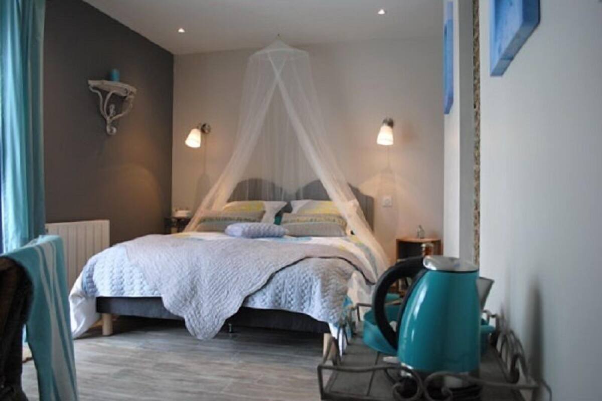 A bedroom with a bed, a canopy, bedside lamps, a chair, and a table with a kettle.