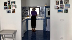 A kitchen with blue tiles, a window, and various photos on the walls.