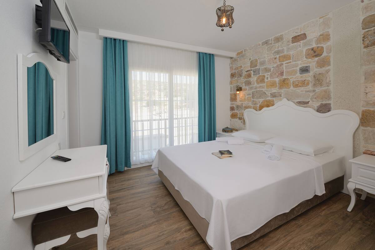 A hotel room with a large bed, a white desk, a TV mounted on the wall, and a stone accent wall.