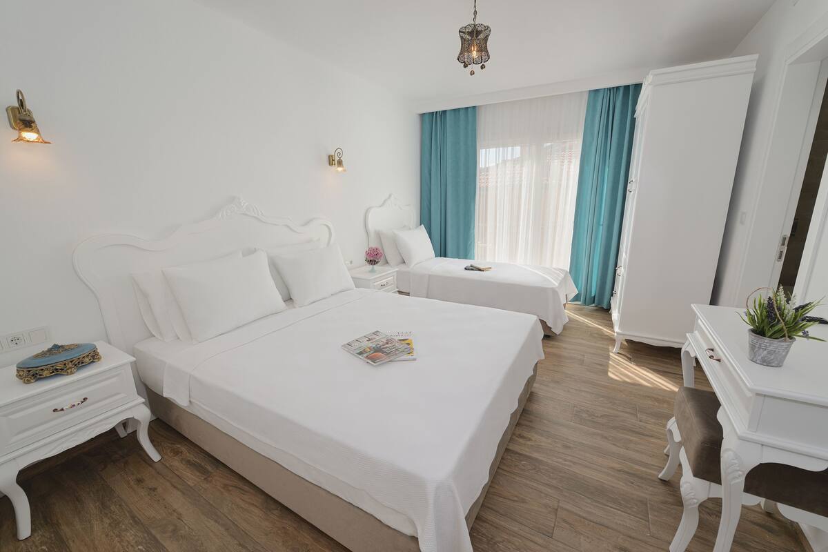 A modern hotel room with a large bed, a smaller bed, a desk, and a wardrobe.