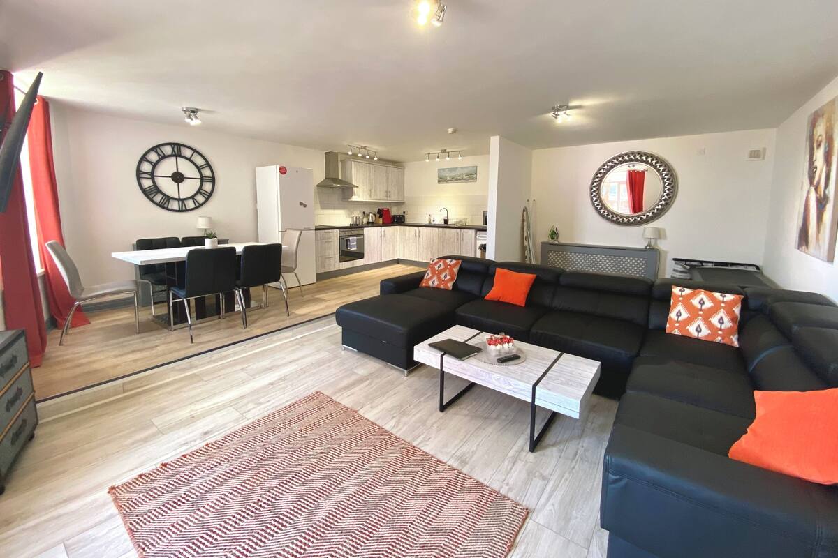 Ein modernes Wohnzimmer mit einem schwarzen Sofa, einem Couchtisch und einem Essbereich mit einem weißen Tisch und Stühlen.