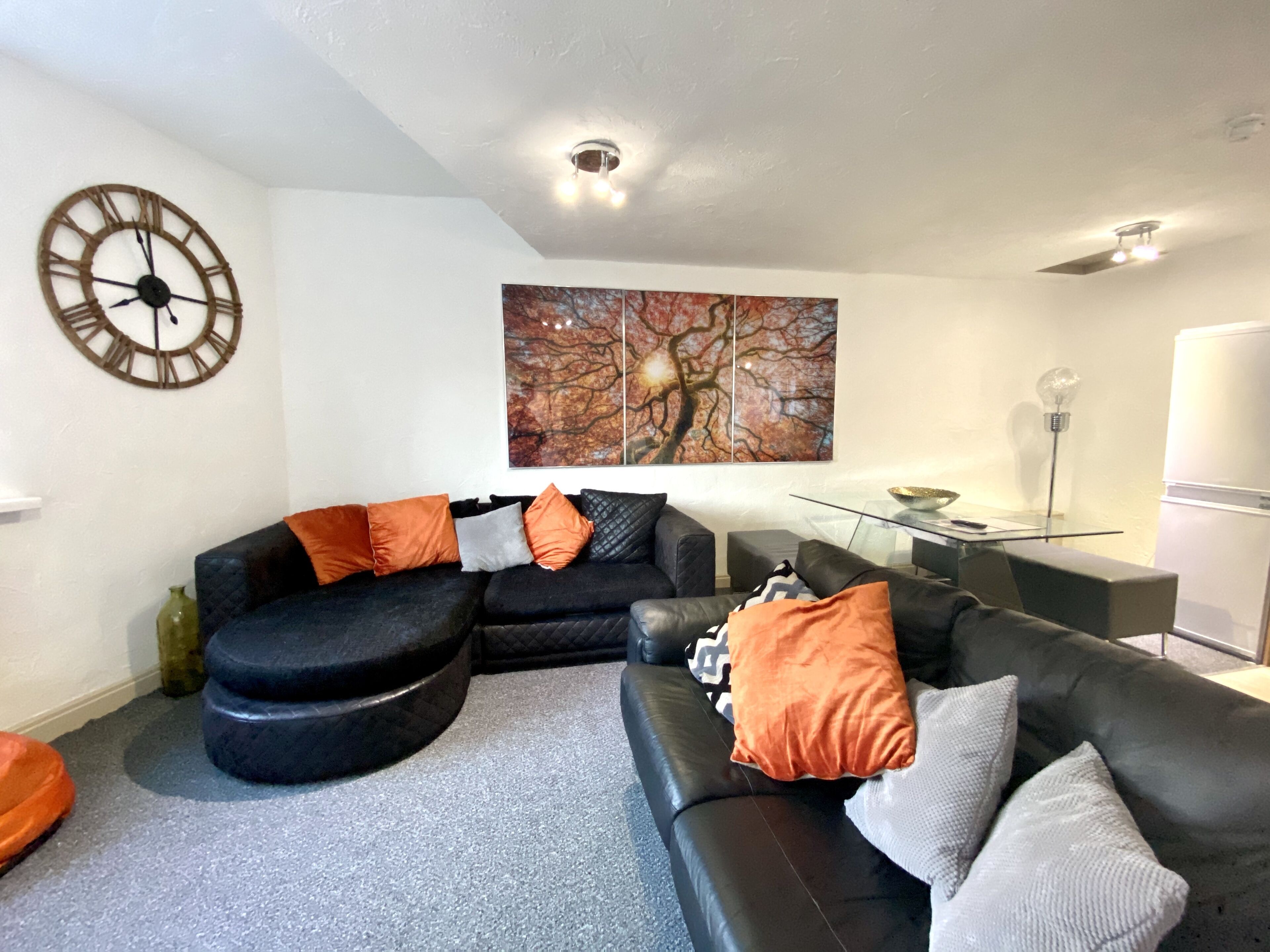 A modern living room with a black sectional sofa, a round wall clock, and a large abstract painting.
