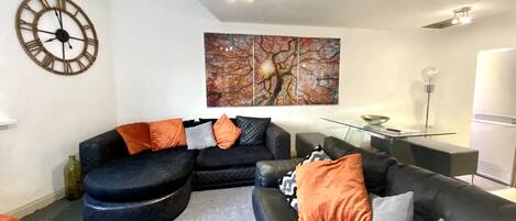 A modern living room with a black sectional sofa, a round wall clock, and a large abstract painting.