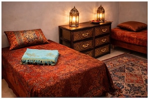 A bedroom with a patterned bedspread, a matching pillow, a nightstand with two lanterns, and a small rug.