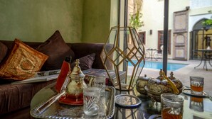 A cozy indoor setting with a sofa, a glass table with tea and glasses, and a view of a pool outside. - Il Parco dei Principi (Marrakech)