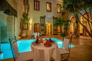 A poolside dining area with a table set for two, surrounded by chairs, and a pool in the background. - Il Parco dei Principi (Marrakech)