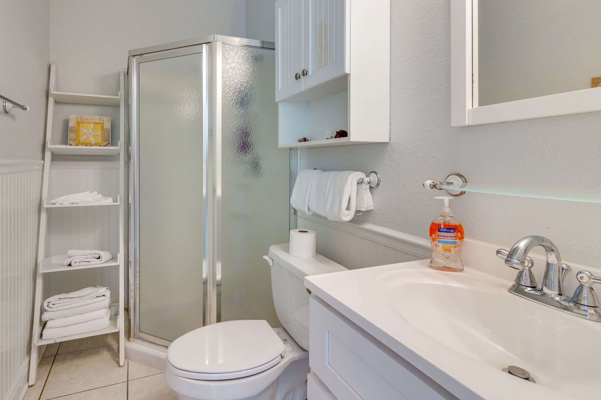 A bathroom with a toilet, a glass shower enclosure, a sink with a mirror, and shelves with towels.