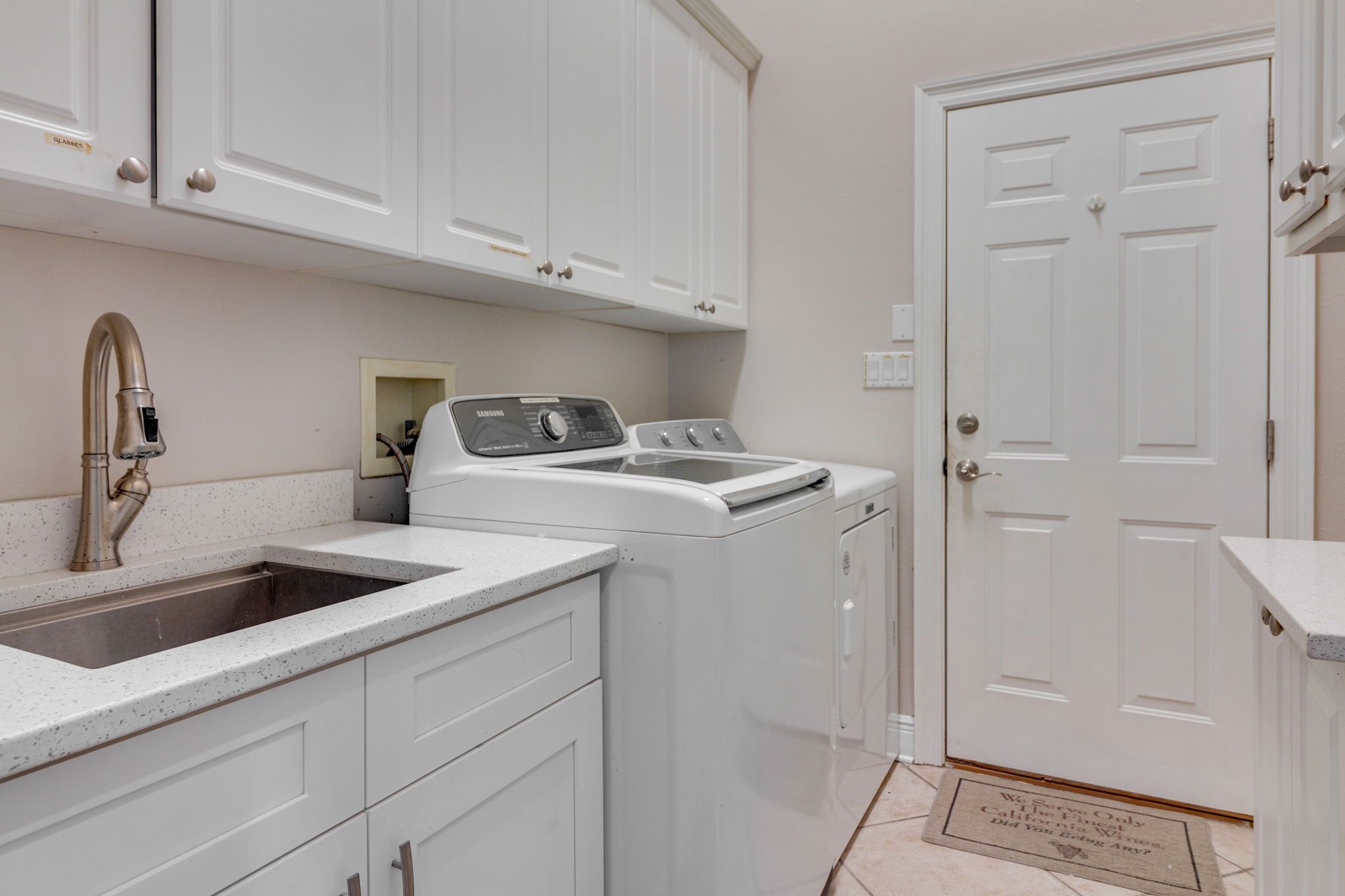 A laundry area with a washing machine, a sink, and white cabinets.
