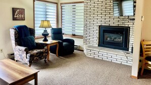 A cozy living room with a fireplace, patterned armchair, and a small table with a lamp. - Cozy 2 Bed, 2 Bath Condo on Golf Course with Hot tub, Sauna & Pool! (Red Lodge)